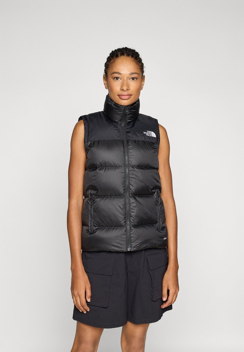 Svart pufferväst med hög krage, dragkedjestängning och sidfickor. Har quiltade sektioner och en logotyp på övre vänstra sidan.