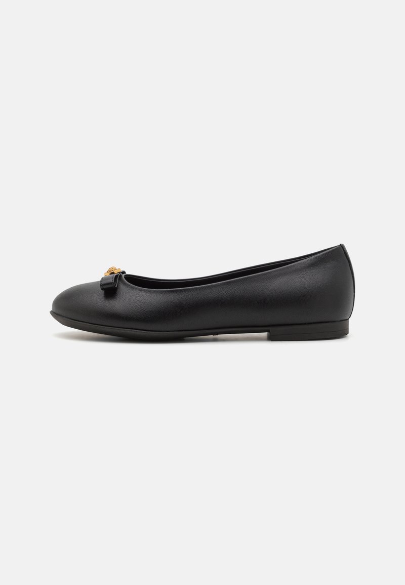 Zapato plano negro de cuero, que presenta una punta redondeada, un pequeño lazo decorativo y un tacón bajo. Textura suave con un diseño minimalista.