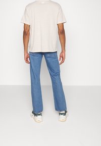 Beżowy t-shirt z krótkim rękawem i jasnoniebieskie jeansy o prostym kroju noszone z białymi trampkami. Strój jest casualowy i charakteryzuje się minimalnymi detalami.