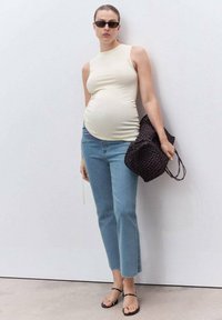 Top sin mangas color beige claro, jeans azules con dobladillo deshilachado, bolso de mano negro tejido, gafas de sol oscuras y sandalias negras con tiras.