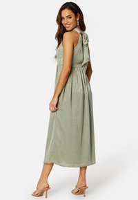 Grön, ärmlös klänning i knälängd med figurnära bodice och plisserad kjol. Mjuk, texturerad tyg med en rosettdetalj på baksidan.