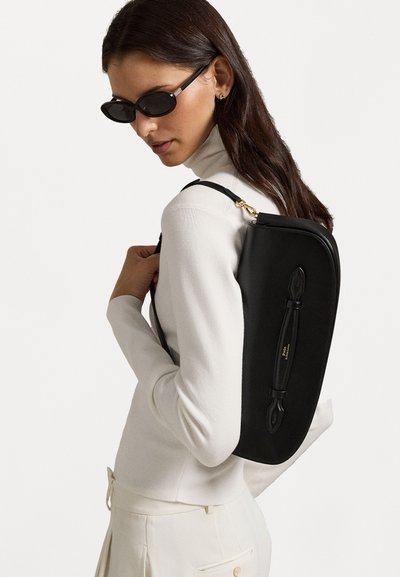 Saco de couro preto com uma forma retangular elegante, apresentando um frente texturizada, ferragens douradas e uma alça de ombro, combinado com um suéter claro.