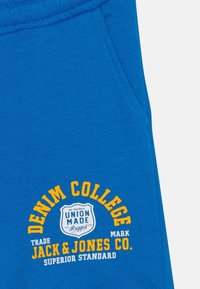 Tessuto blu con una tasca, caratterizzato da una stampa gialla e bianca che recita "Denim College, Jack & Jones Co., Union Made, Superior Standard."