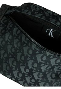 Borsa nera in tessuto Calvin Klein con motivo a logo ripetuto, dotata di chiusura con zip e fodera interna liscia, che mette in risalto dettagli di design testurizzati.