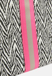 Plátěná taška s černobílým cikcak vzorem, doplněná výrazným růžovým a šedým proužkem. Texturovaný materiál přidává vizuální zajímavost.