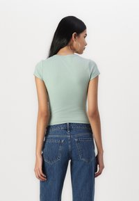 Top scurt cu maneci scurte, de culoare verde mentă, asortat cu blugi din denim albastru cu talie înaltă; material fin, cu un design minimalist și fără modele vizibile.