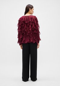 Burgundy blouse with layered ruffles at the back, paired with black wide-leg pants. Smooth texture and loose fit.