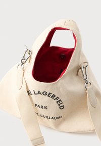 Geantă din pânză bej Karl Lagerfeld Paris Saint-Guillaume, cu interior roșu, mâner superior, curea detașabilă și închidere cu buton tip snap.