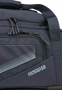 Borsone di un blu navy scuro con tessuto testurizzato, dotato di più scomparti con zip, strisce azzurre a contrasto e una maniglia rinforzata.
