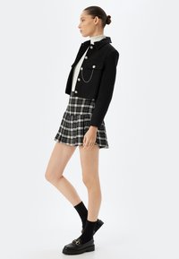 Giacca nera corta con bottoni argentati, abbinata a una minigonna a quadri bianco e nera. Il modello indossa calzini neri e mocassini chunky.