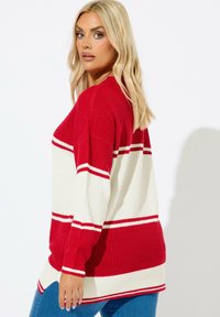 Punainen ja valkoinen raitaneulepusero, jossa on pitkät hihat, ribbitekstuuri ja sivureiät helman kohdalla. Rennon mallinen, näkyviä ompelutekstiilejä.