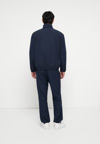 Jūrinis treningas su užtrauktuku ir elastingomis rankovėmis, pasižymintis laisvu kirpimu. Balti sportbačiai puikiai papildo aprangą. Paprastas dizainas, be raštų.