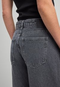 Striped grey jeans featuring a high waistband, two back pockets with stitched accents, and a black leather tag on the waistband.
