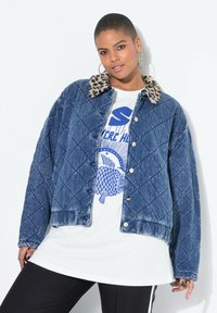 Kurtka dżinsowa pikowana w ciemnym niebieskim kolorze z kołnierzem z futra w panterkę, z srebrnymi zatrzaskami i luźnym krojem. Noszona na koszulce z nadrukiem.