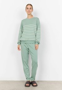 Ensemble de détente vert clair comprenant un haut à rayures à manches longues et un pantalon fuselé assorti, fabriqué en tissu doux. Sandales à glissière brunes incluses.
