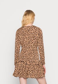 Vestido de padrão de leopardo em bege, com mangas longas, bainha com volantes e material elástico. Apresenta um corpete ajustado e uma silhueta ampla.