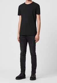 Musta puuvillapaita pyöreällä kaula-aukolla, yhdistettynä slim-fit mustiin farkkuihin, joissa on hienovaraisia kulutuksia. Vahvat mustat nauhakenkä bootsit.