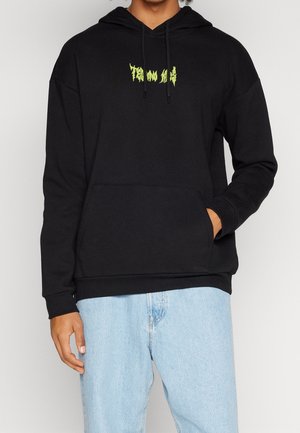 Sudadera negra de algodón, con cordón y un bolsillo canguro. Tiene un logo gráfico verde prominente en el pecho.