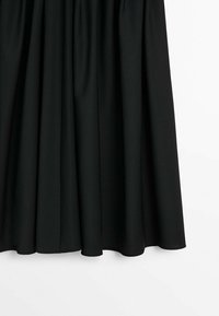 Jupe plissée noire suspendue avec un ourlet légèrement évasé sur fond blanc.