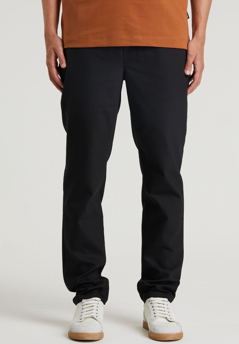 Svarta byxor med rak ben-design, robust tyg och slät textur, i kombination med vita sneakers.