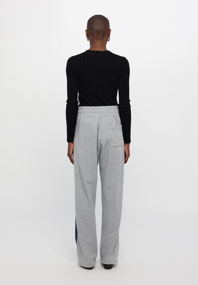 Pantalones de chándal grises con cinturilla elástica y detalles en las costuras laterales, combinados con una camiseta de manga larga de canalé negra. Diseño simple, estilo casual.