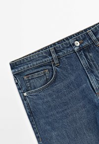 Partie taille d’un jean en denim bleu foncé avec poche avant, passants de ceinture et bouton argenté sur fond blanc.
