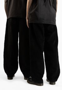 Pantaloni a gamba larga in corduroy nero con tessuto strutturato, abbinati a calzature nere. Le maglie sono morbide e anch'esse di colore nero.