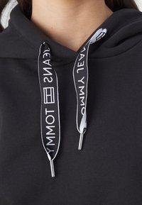 Black hooded sweatshirt with white drawstrings featuring logo text. Soft fabric, ribbed texture at the cuffs and hem.