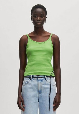 Groene geribde tanktop met brede schouderbanden, gecombineerd met lichtblauwe high-waisted jeans met een zwart trekkoorddetail in de taille.