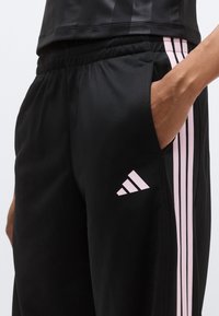 Μαύρο αθλητικό παντελόνι με ροζ ρίγες και λογότυπο adidas. Διαθέτει κλασική εφαρμογή, ελαστική μέση και πλαϊνές τσέπες για ευκολία.