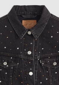 Zwarte denim jas met een klassieke kraag, versierd met zilveren en gouden pailletten. De voorkant heeft twee borstzakken met metalen details.