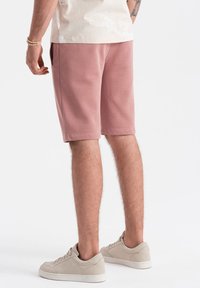 Světle růžové teplákové šortky vyrobené z měkké látky, s elastickým pasem a bočními kapsami, spárované s béžovými teniskami.