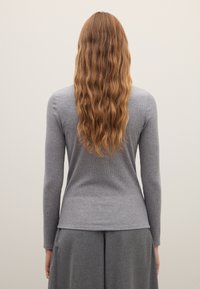 Graues Langarmoberteil mit geripptem Muster, figurbetontem Schnitt und dezentem Saumdetail, kombiniert mit einem grauen Rock, von hinten gesehen.