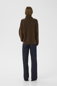 Hnědý, oversized rolák s měkkou texturou, kombinovaný s tmavě modrými džínami rovného střihu. Jednoduchý, minimalistický design bez viditelných detailů.