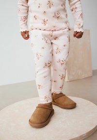 Helles rosa, geripptes Baumwolloutfit mit Blumenmuster, das an der Oberseite mit Rüschen versehen ist und eng anliegende Hosen hat. Braune Wildleder-Slipper.