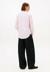 Light pink long-sleeve shirt with subtle textured patterns, paired with dark wide-leg jeans; shirt features a curved hem and collar.