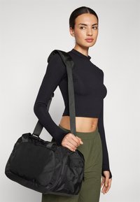 Black duffel bag made of durable fabric, featuring a shoulder strap and multiple compartments for storage. Compact design with smooth texture.