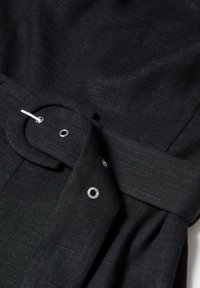 Robe en lin noire dotée d'une large ceinture avec une boucle circulaire. Ferrures métalliques argentées avec œillets et texture lisse.