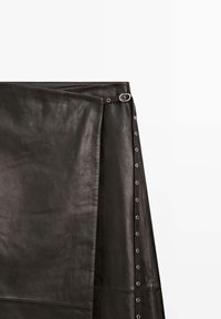 Schwarzer Lederrrock mit glatter Textur, seitlicher Verschluss mit silbernen Ösen und dekorativem Ringakzent.