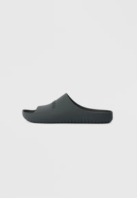 Μαύρη σαγιονάρα από καουτσούκ. Διαθέτει λεία επιφάνεια, ανοιχτό μπροστινό μέρος και ραβδωτή σόλα. Λογότυπο αποτυπωμένο στο πλάι.