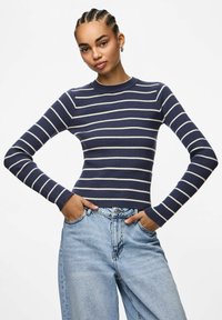 Marinblå randig långärmad ribbad topp med rundad hals, ihop med ljusblå denimjeans. Toppens design har växelvis vita ränder.