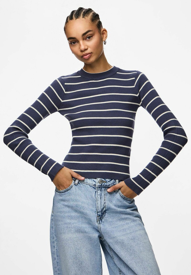 Marinblå randig långärmad ribbad topp med rundad hals, ihop med ljusblå denimjeans. Toppens design har växelvis vita ränder.