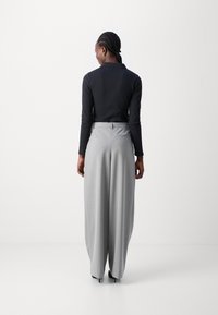 Haut noir à manches longues associé à un pantalon large gris clair. Le pantalon présente une taille haute et des détails de poches subtils.