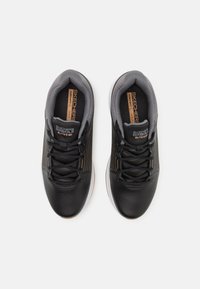 Fekete sportcipők texturált szintetikus felsőrésszel, kontrasztos szürke béléssel és minimalista dizájnnal; vékony fűzőkkel és gumi talppal rendelkezik.