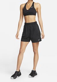 Musta urheilullinen crop top kietaisumallilla, yhdistettynä mustiin shortseihin, joissa on joustava vyötärö. Mustat tennarit täydentävät asun.