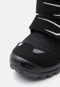 Μαύρο αθλητικό παπούτσι με υφασμάτινη πάνω επιφ�άνεια με υφή, λουράκια Velcro και ανθεκτική καουτσούκ σόλα. Σημαντικές ανακλαστικές λεπτομέρειες και γκρι λεπτομέρειες.