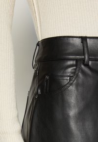 Jupe en cuir noir à texture lisse, taille haute, coutures visibles et poches latérales. Stylisée avec un haut en maille de couleur claire.