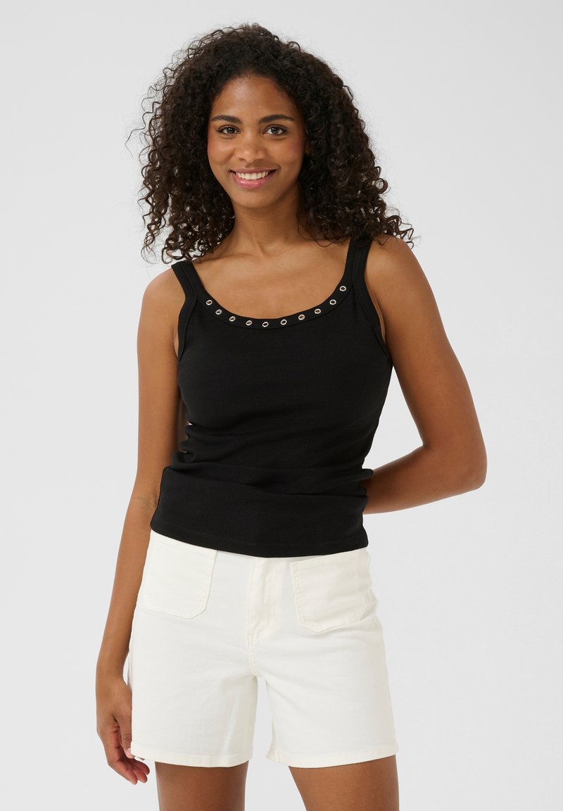 Débardeur noir côtelé avec un décolleté rond et des œillets métalliques décoratifs. Assorti à un short en denim blanc, mettant en avant des poches avant.