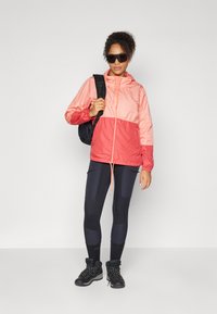 Lightweight, two-tone pink windbreaker with a hood, elastic cuffs, and drawstring hem. Paired with black leggings and black hiking boots.