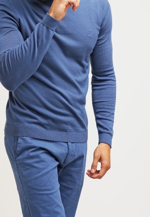 Blauer Strickpullover mit langen Ärmeln und Rundhalsausschnitt, kombiniert mit passenden blauen Hosen. Leichte Textur auf dem Stoff sichtbar.